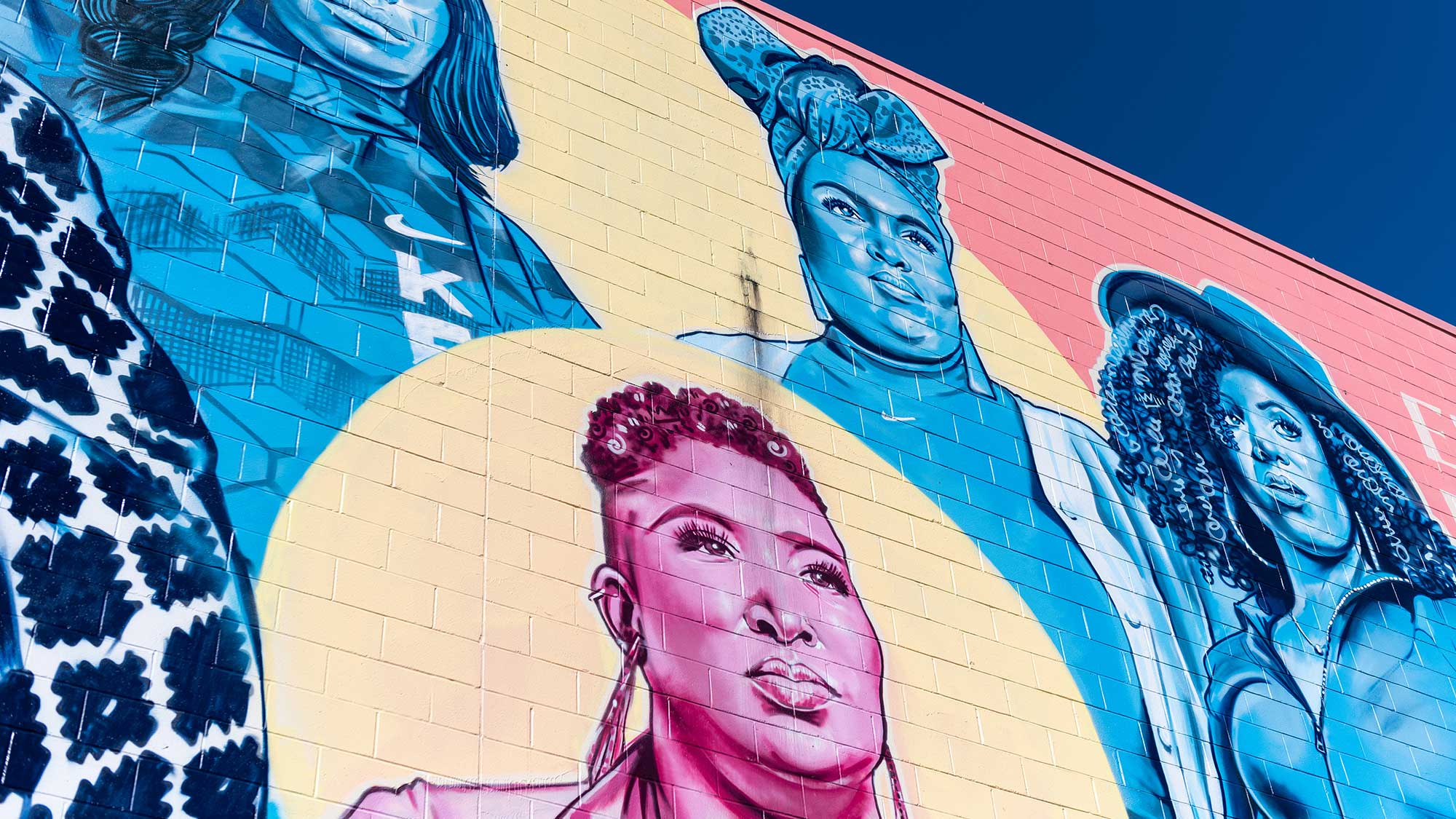 A yellow, blue and pink painted mural on a brick wall