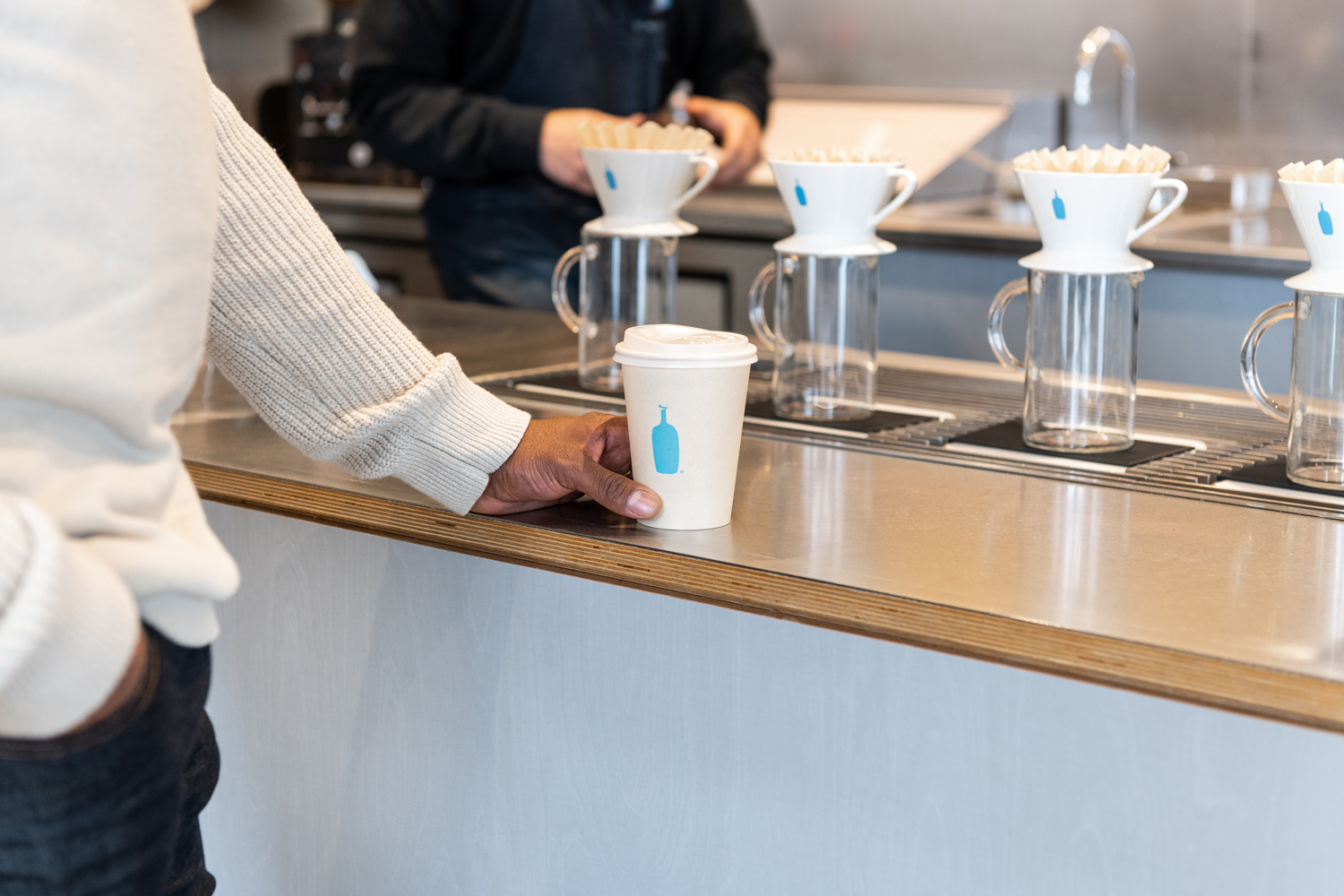 A man holding a to-go cup of coffee at Blue Bottle Cafe