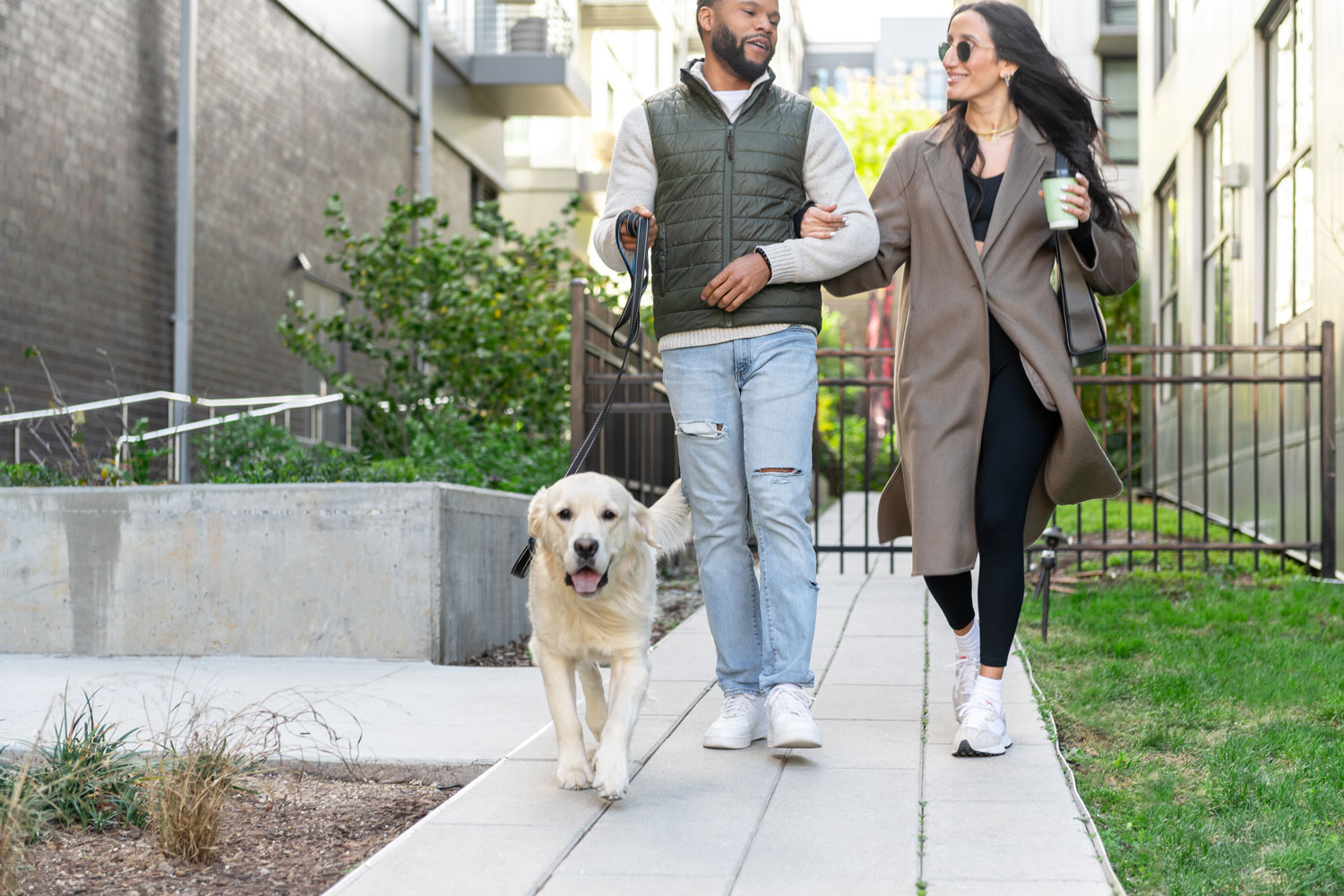A young couple walking their dog outside on a sidewalk