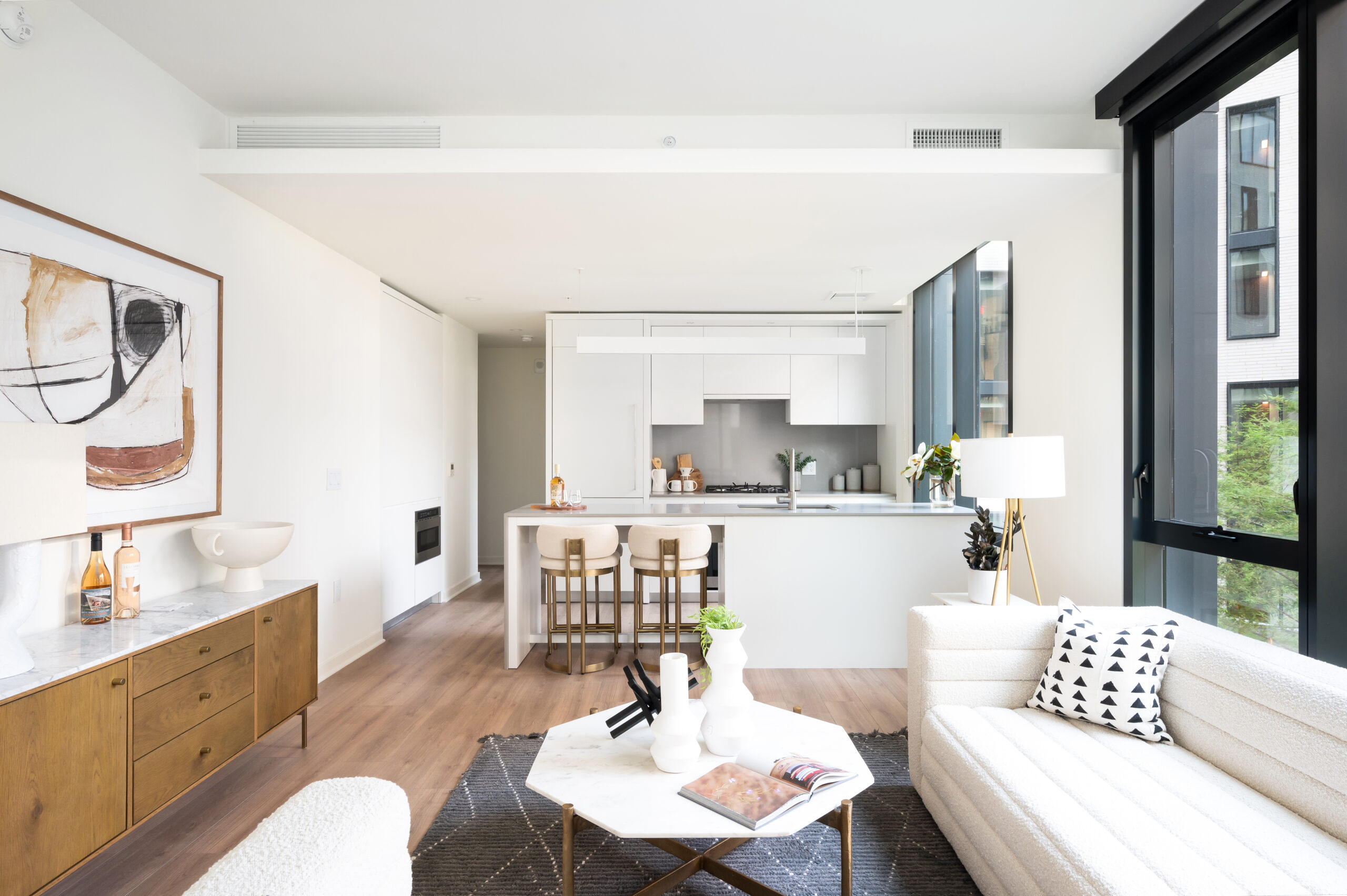 Margarite luxury apartments' living room & kitchen in Washington, DC, with white furniture, wooden floors, & large windows.